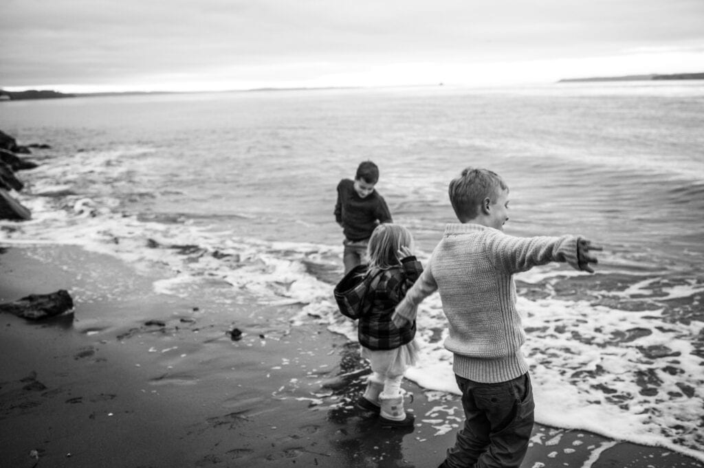 three children play on the beach at Point No Point. They are all facing the water.