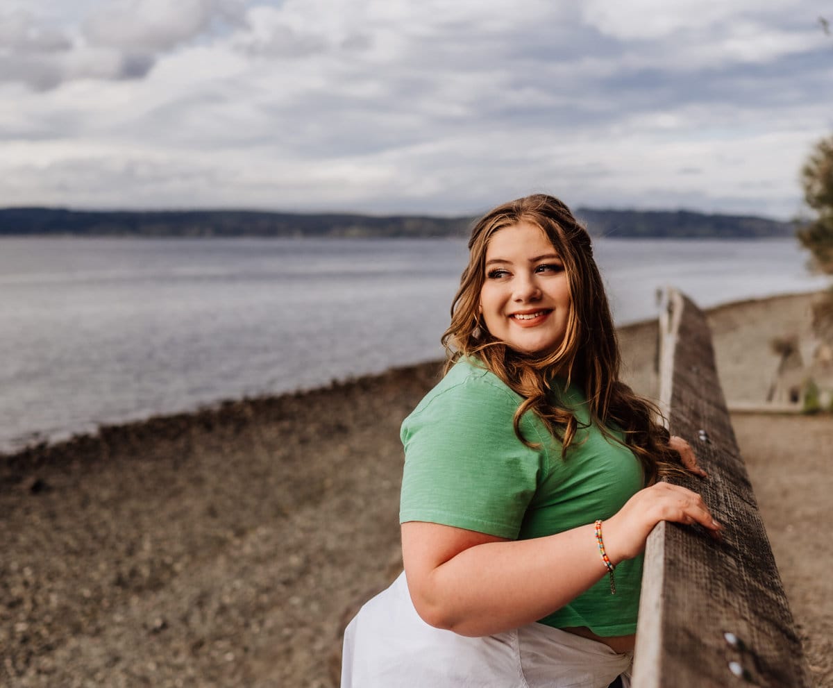 A young woman looks away from the camera while holding onto a rail at Kitsap Memorial Park. The beach is in the beackground