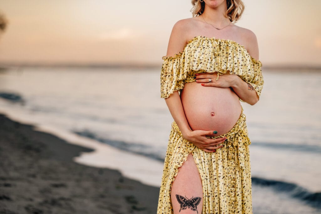 A pregnant woman in a yellow dress with a tattoo on her leg