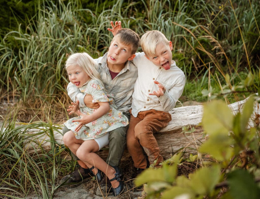 Three young siblings, 2 boys and 1 girl, make silly faces during a family portrait session