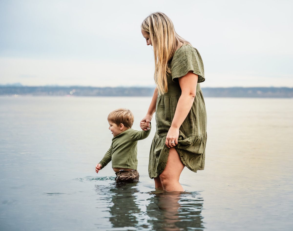 A mother and her son walk through the water at a beach in Kingston