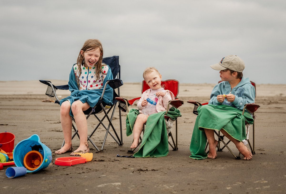 Three children enjoying a day at the beach with sand toys, snacks, and comfortable chairs.