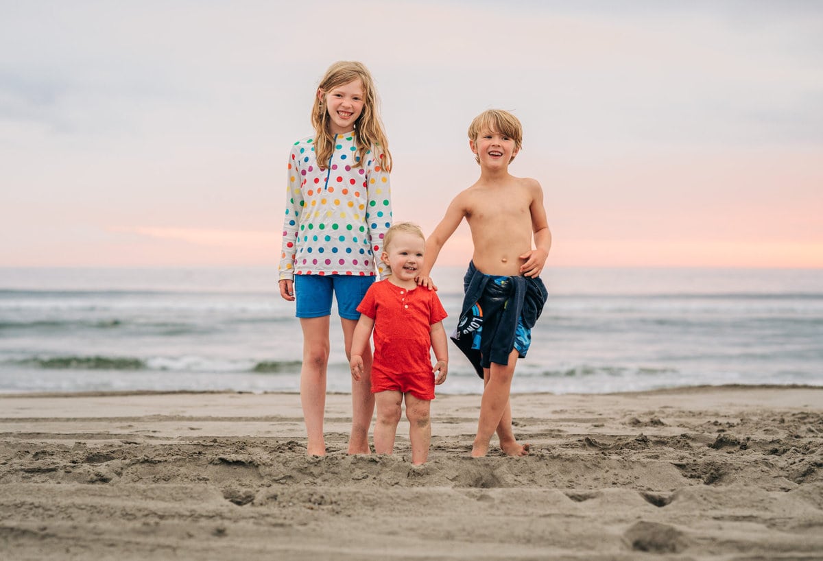 Three children smiling on the beach at sunset.